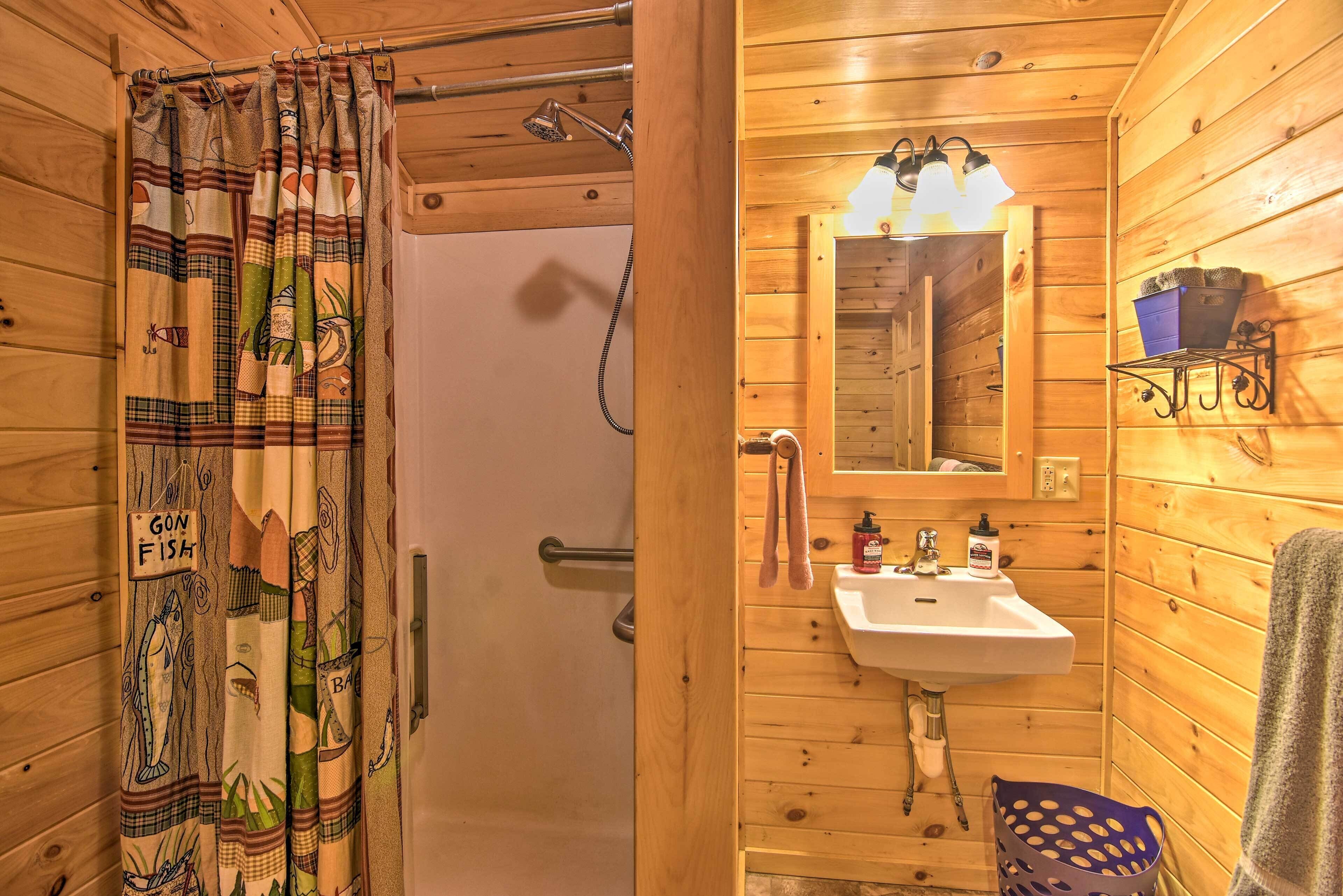 Bagno di una baita in legno con tenda da doccia, lavandino, specchio e ripiano con articoli da toilette.