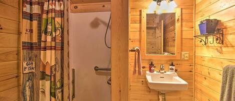 A wooden cabin bathroom with a shower curtain, sink, mirror, and a shelf with toiletries.