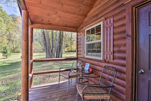 A wooden cabin with a porch, two metal chairs, a small table, and a window. - Rural Cabin Hideaway w/ Fire Pit & Mtn Views! (Parsons)