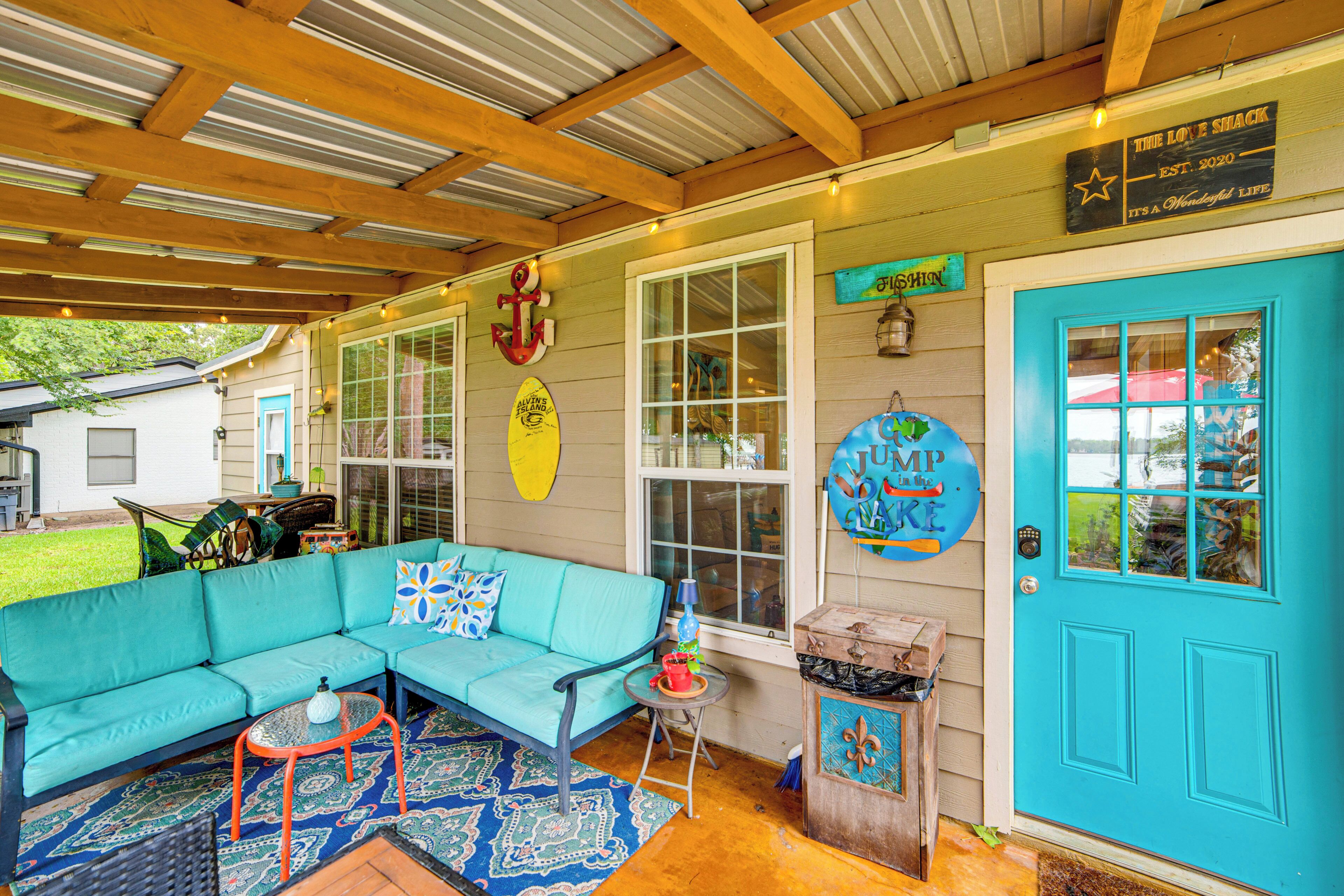 A covered outdoor seating area with a turquoise sofa, a small table, and a blue door.