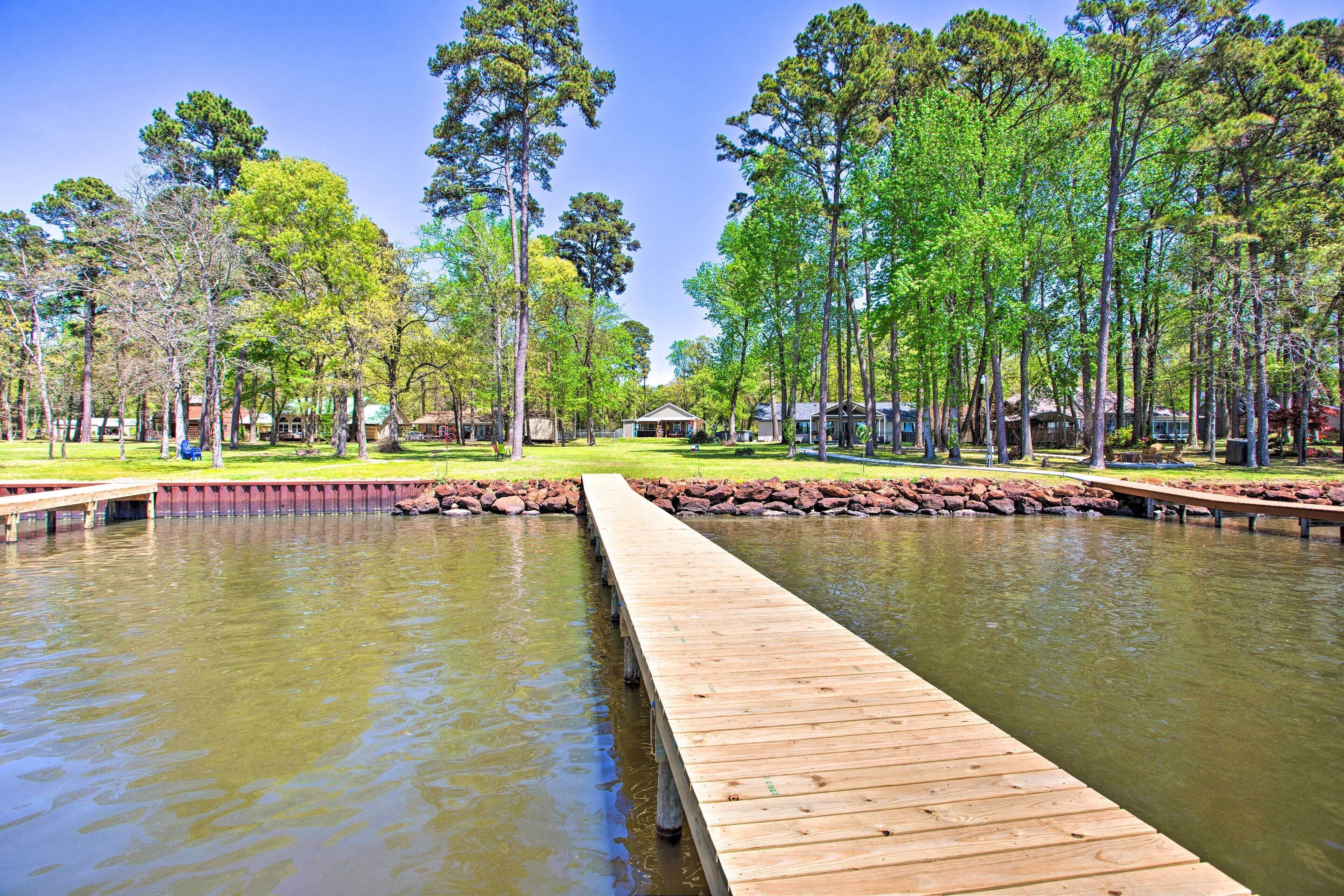 A wooden pier extending into a calm body of water, surrounded by lush greenery and tall trees.