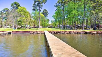 A wooden pier extending into a calm body of water, surrounded by lush greenery and tall trees.