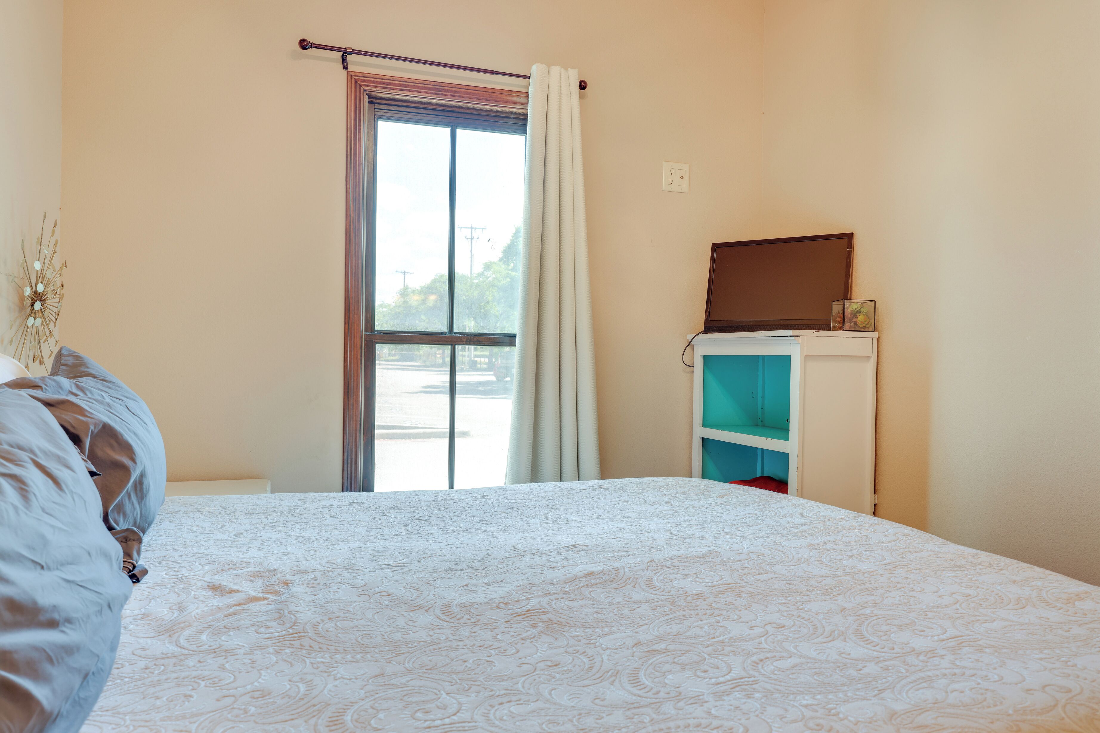 Une chambre à coucher avec un lit, une fenêtre avec des rideaux, une étagère avec un cadre photo et une porte.