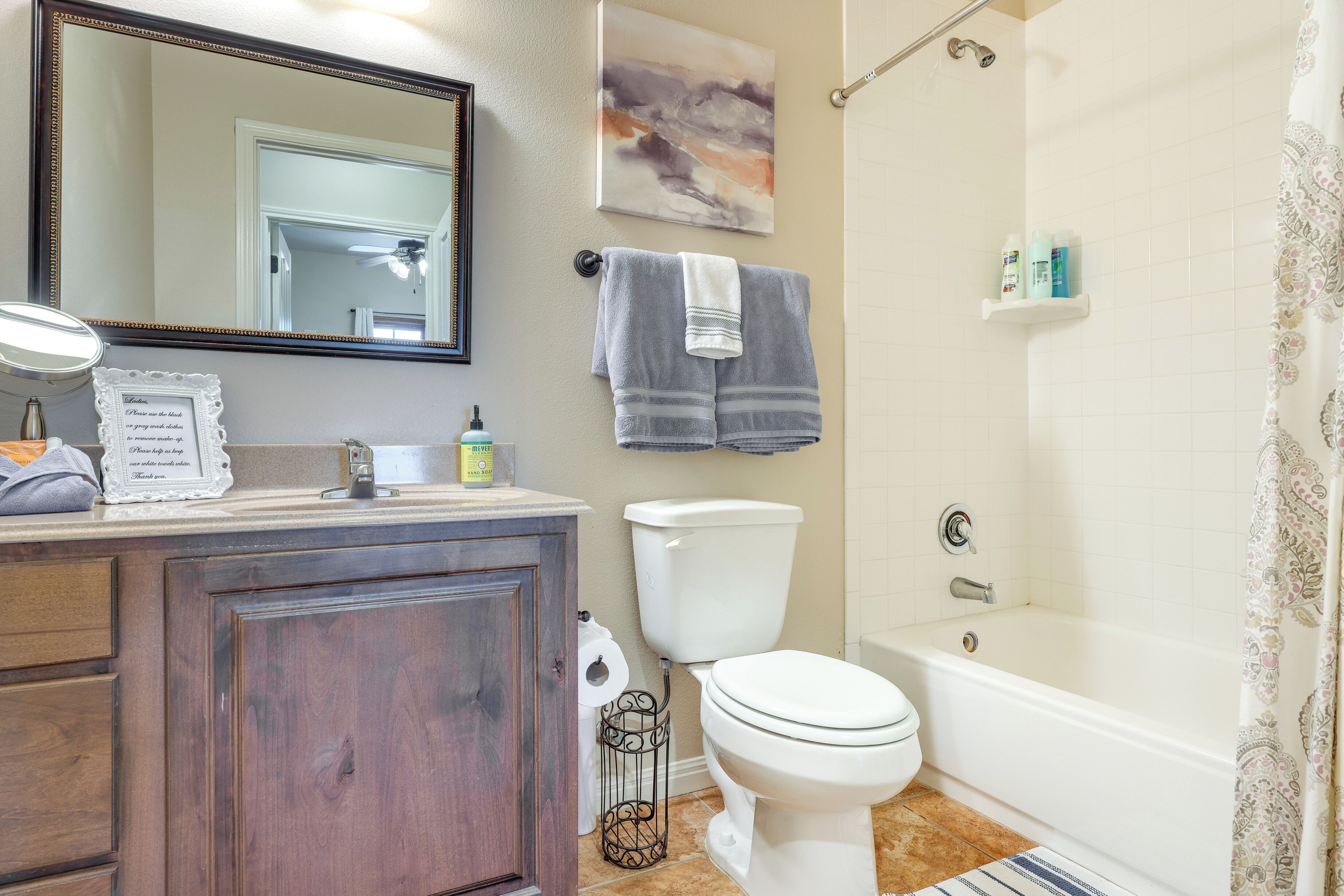 Un baño con tocador de madera, inodoro blanco, bañera y cortina de ducha.