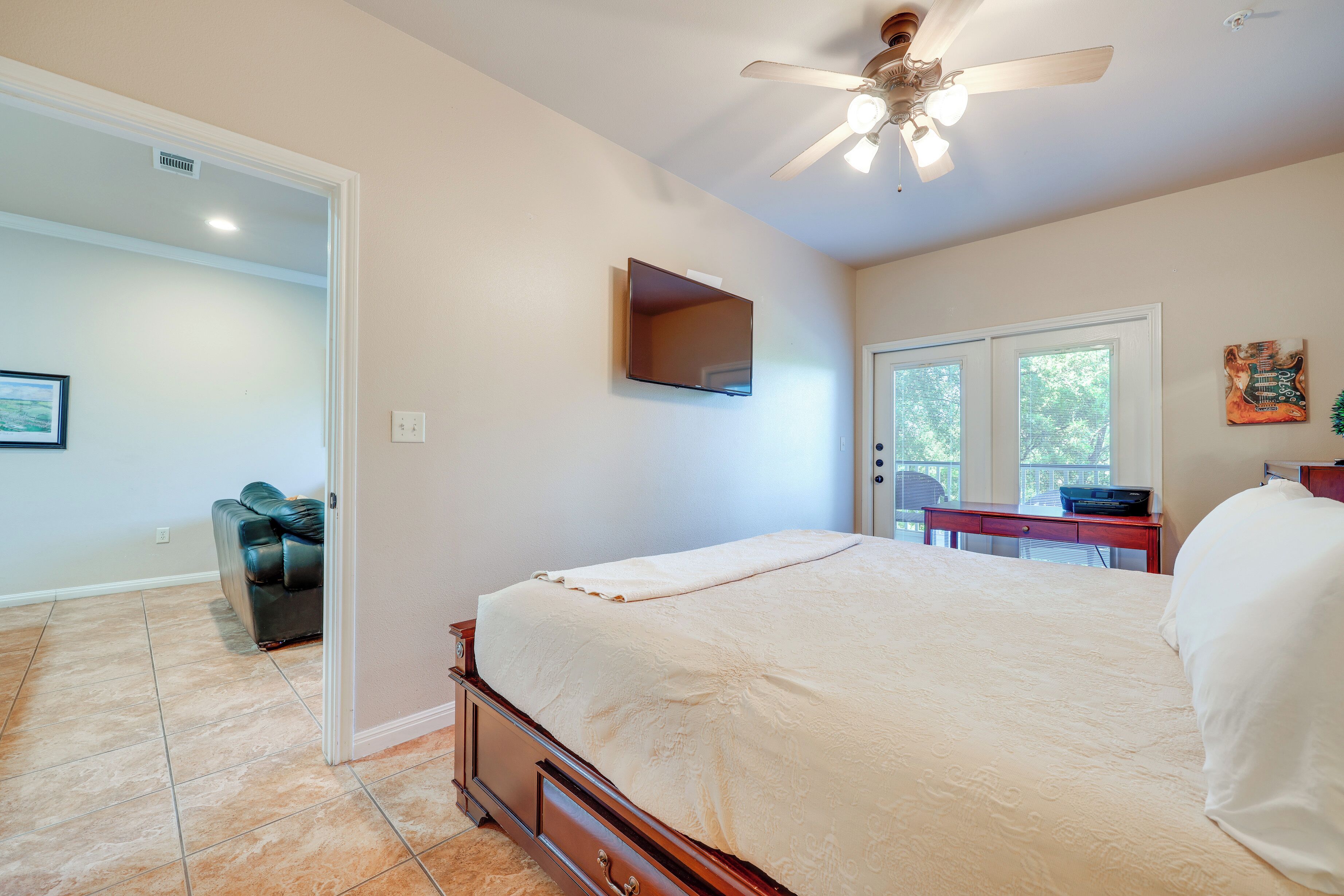 Une chambre à coucher comprenant un lit, un ventilateur de plafond, un téléviseur fixé au mur et une porte donnant sur une autre pièce.