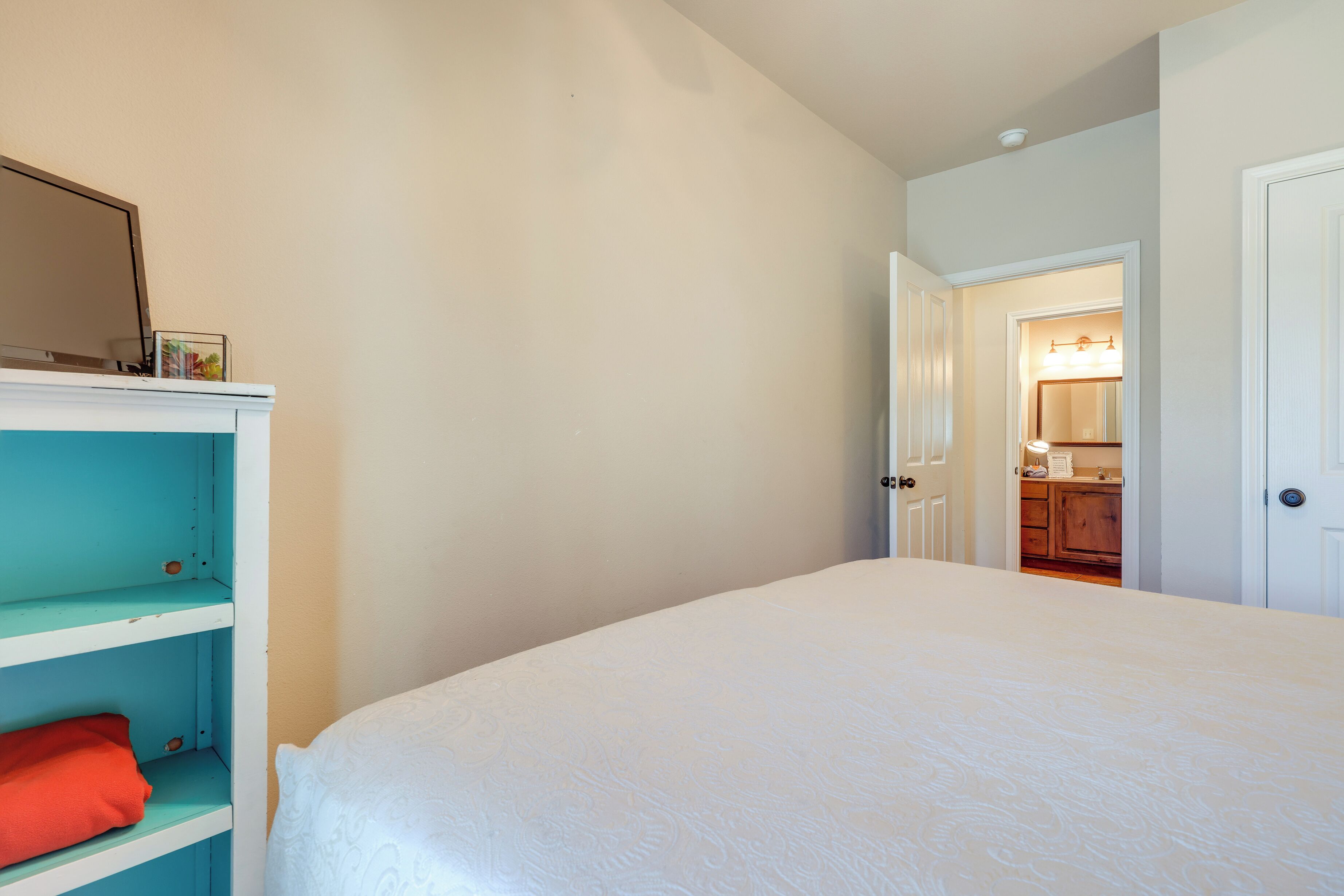 Une chambre avec un lit, une étagère de couleur turquoise et une porte donnant sur une salle de bain.