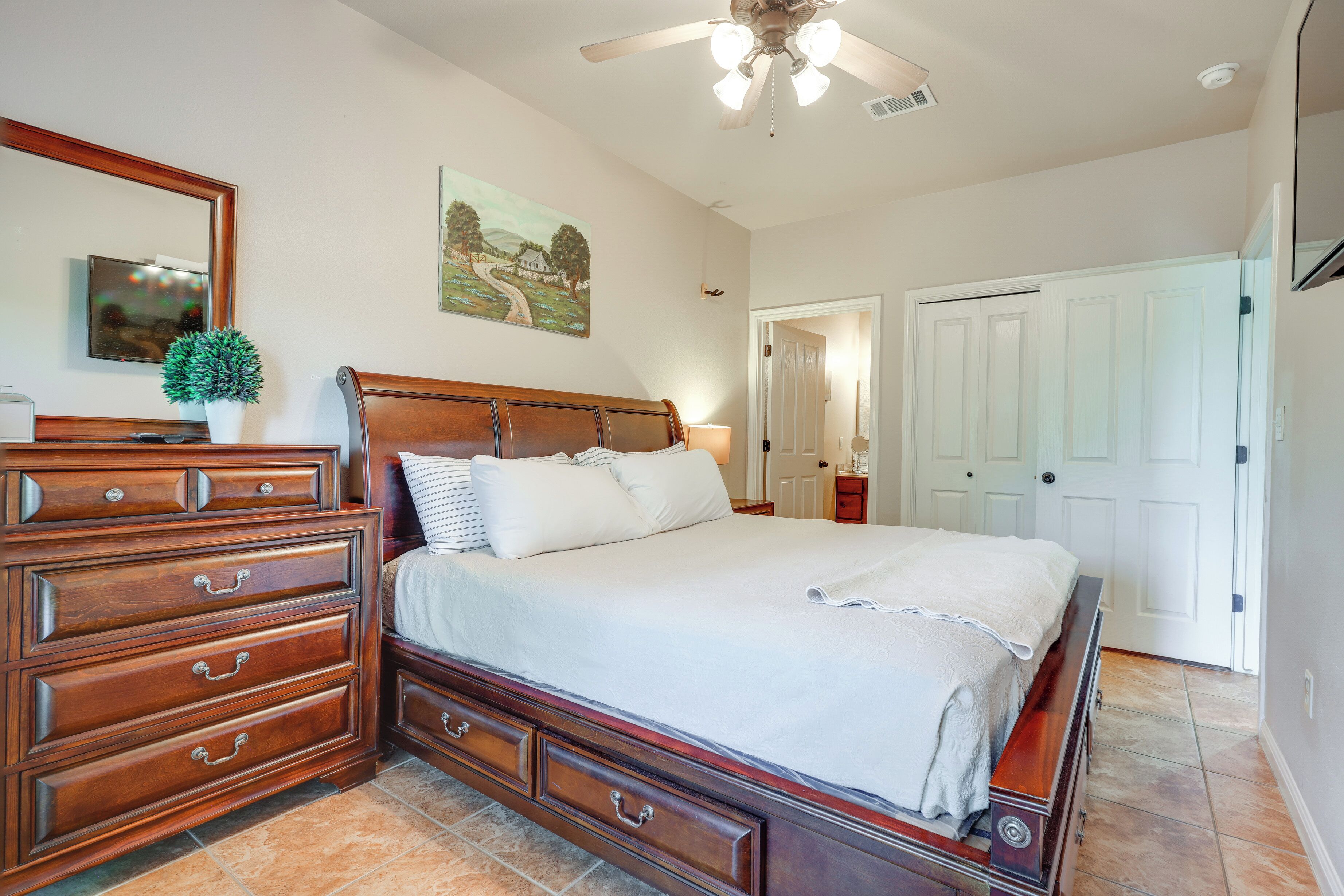 A bedroom with a large bed, wooden dresser, and a ceiling fan.
