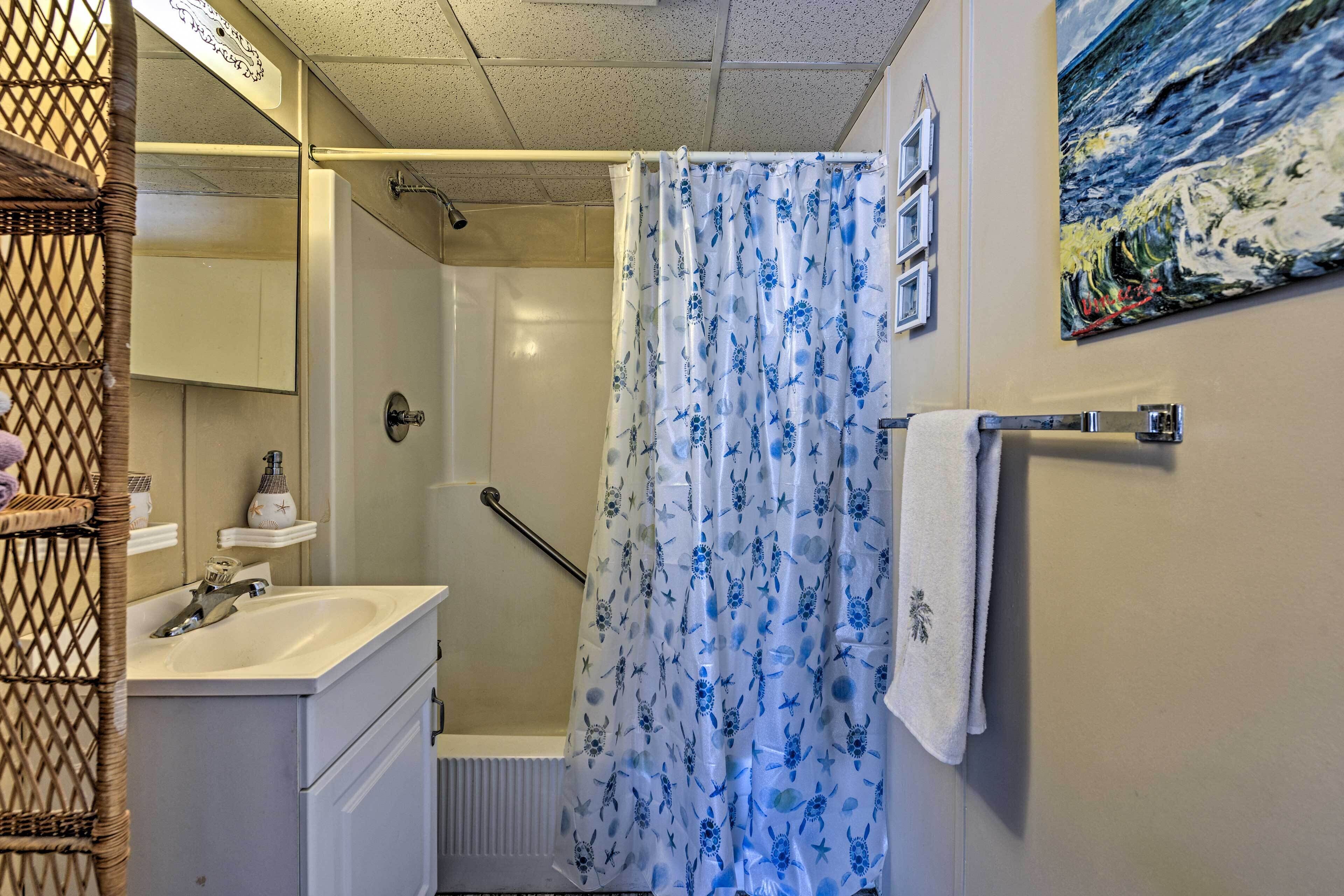 A bathroom with a shower curtain, a sink, a mirror, and a towel rack.