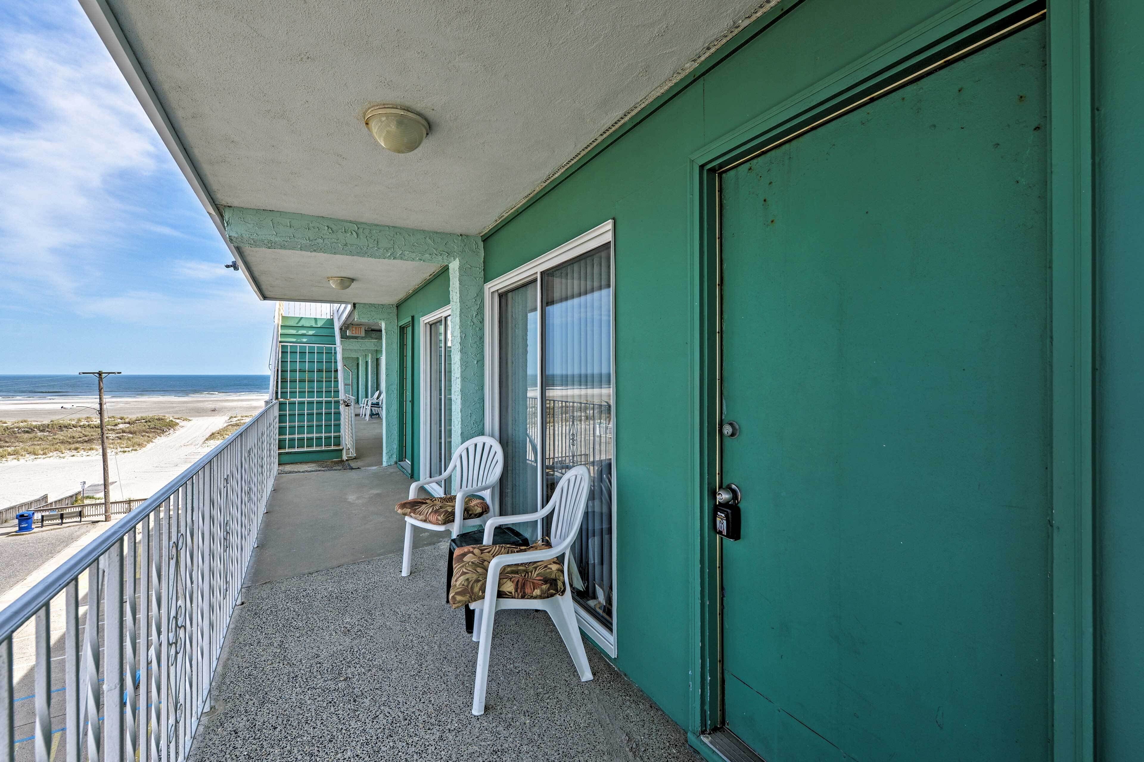 A balcony with two white plastic chairs and a green door.