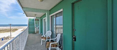 A balcony with two white plastic chairs and a green door.
