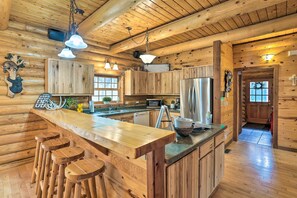 A wooden cabin interior with a kitchen area featuring a bar, stools, and a refrigerator. - Piedmont Cabin ~ 10 Mi to Rapid City! (Piedmont)