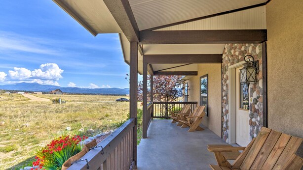 A covered porch with wooden chairs, a stone wall, and a view of a grassy field and mountains. - 2 Mi to Hot Springs: Nathrop Gem w/ Fire Pit (Nathrop)