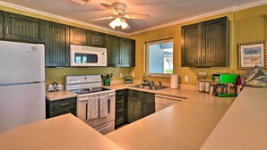 A kitchen with dark wooden cabinets, a white refrigerator, a microwave, a stove, and a ceiling fan. - Bright Coastal Condo: Walk to Lido Key Beach! (Sarasota)