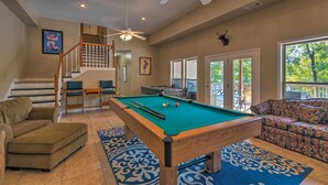 A pool table in a living room with a staircase, a sofa, and a view of the outdoors. - Home on Lake Catherine w/ Dock 9 Mi to Hot Springs (Hot Springs)