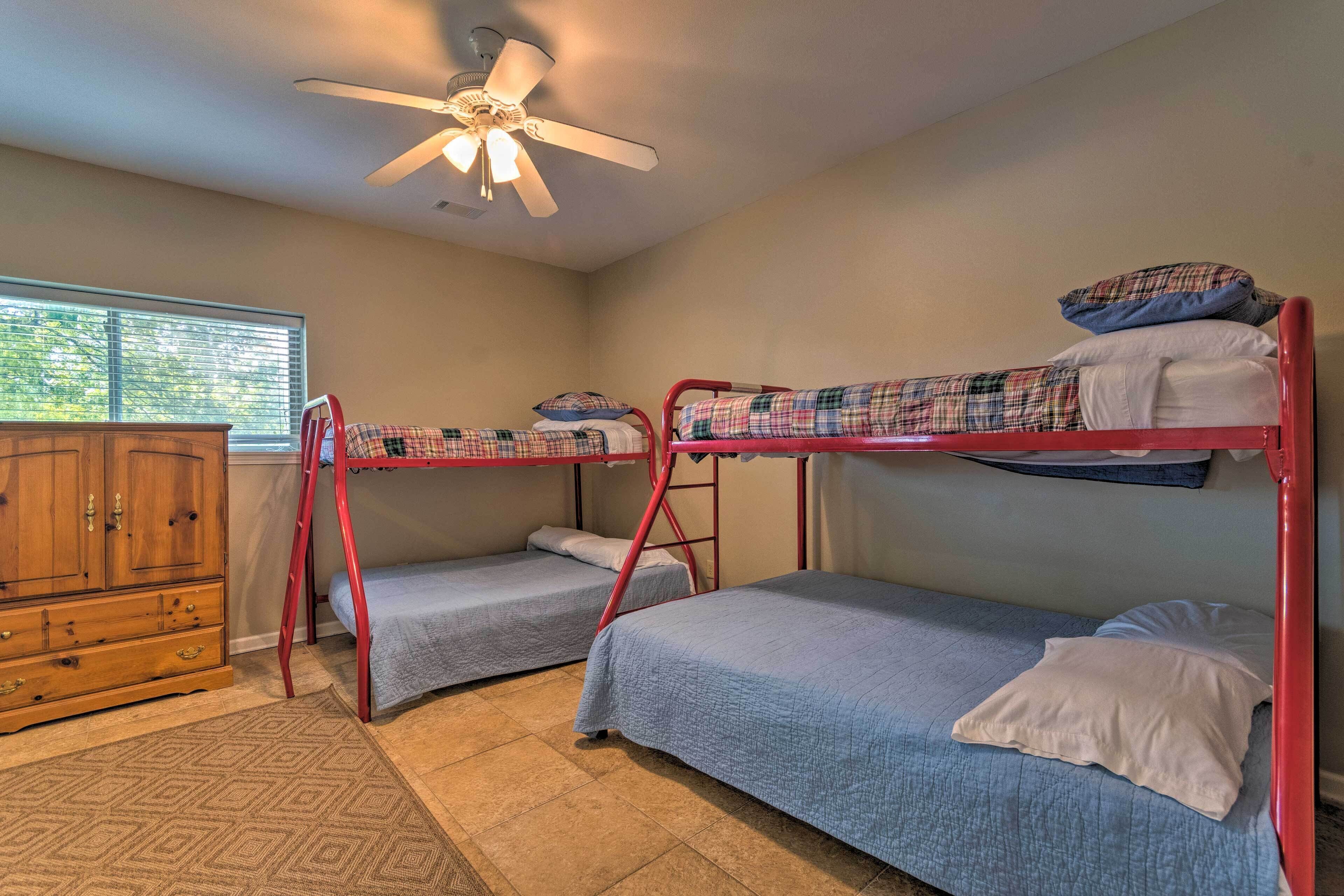 A dormitory room with bunk beds, a wooden dresser, and a ceiling fan.