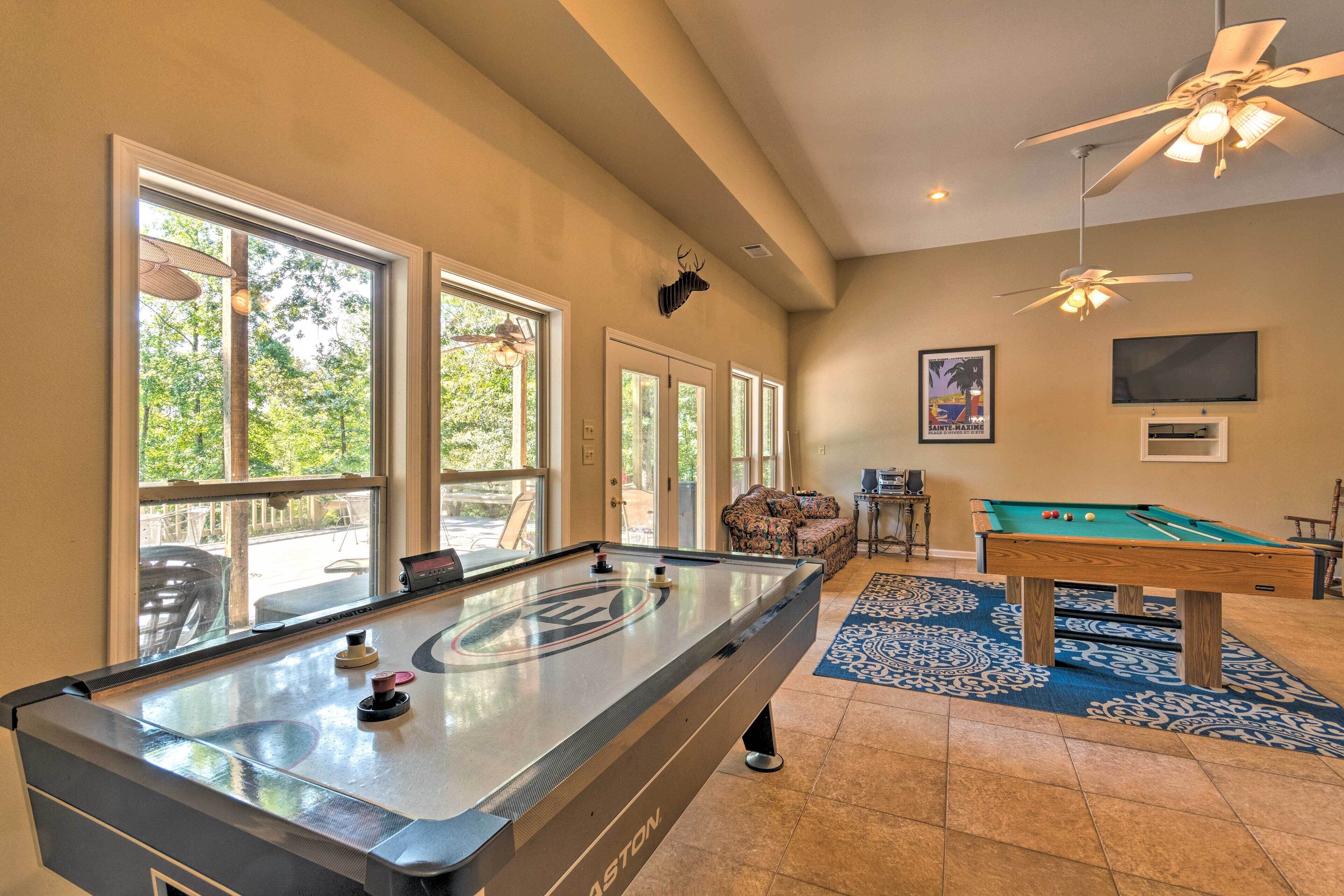 A pool table in a room with large windows, ceiling fans, and a blue patterned rug.