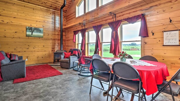 A cozy cabin interior with a dining area, a fireplace, and large windows offering a view of the outdoors. - Cozy Haven of Rest Home w/ Amish Country Views! (Shipshewana)