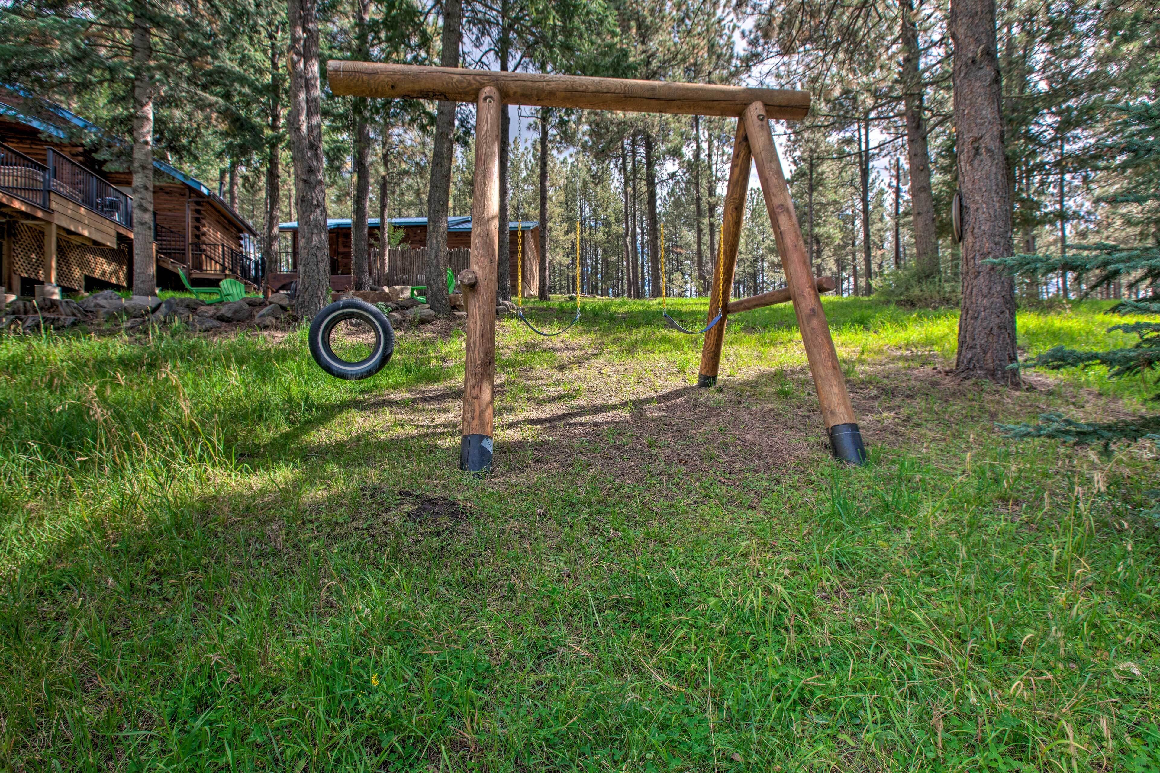 Un conjunto de columpios de madera en un área boscosa, con una cabaña al fondo.