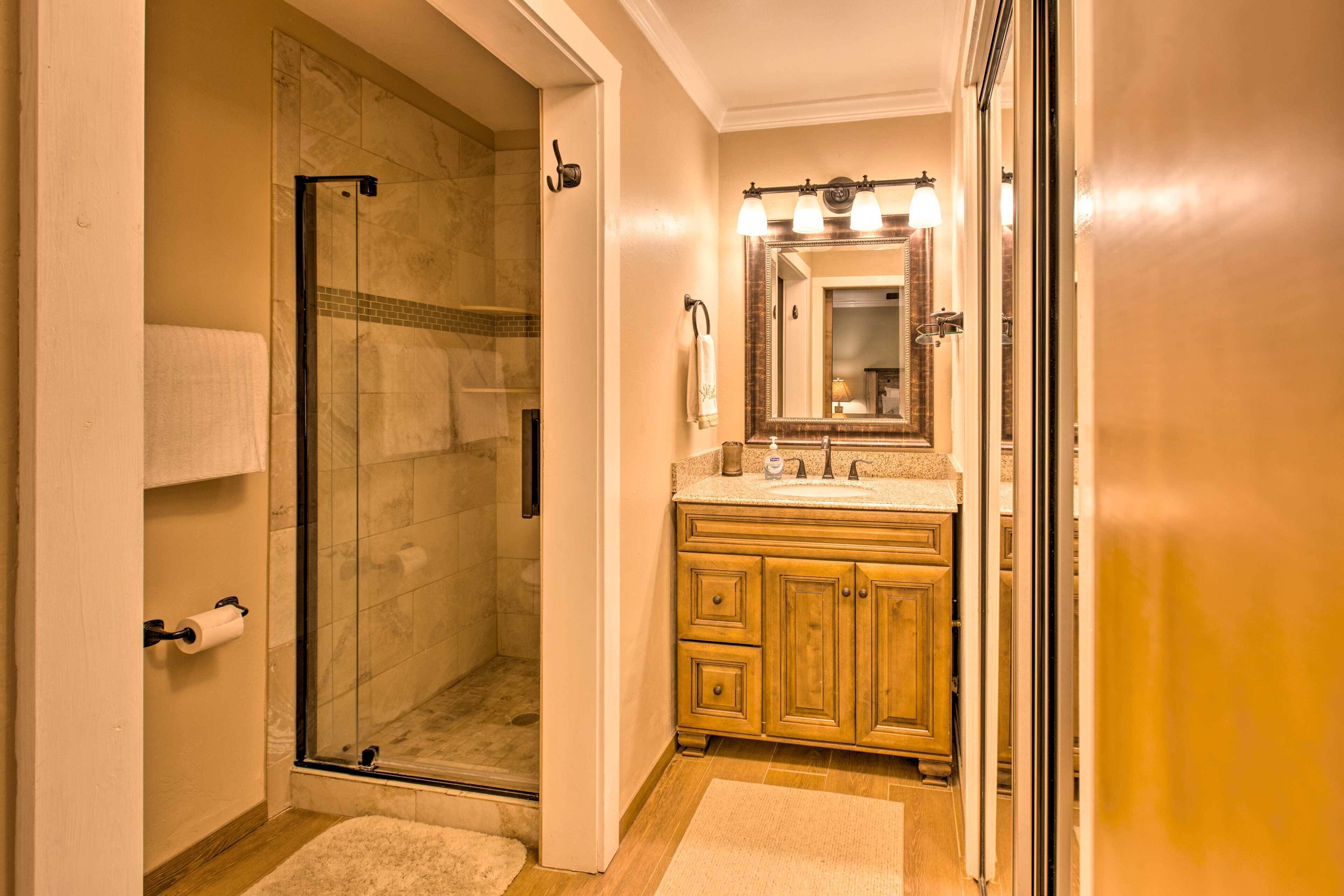 A bathroom with a glass-enclosed shower, wooden cabinets, and a vanity with a mirror and lights.