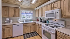 A kitchen with wooden cabinets, a dishwasher, a microwave, a stove, and a window with a curtain. - Rustic Bullhead City Retreat w/ Porch & Views (Bullhead City)