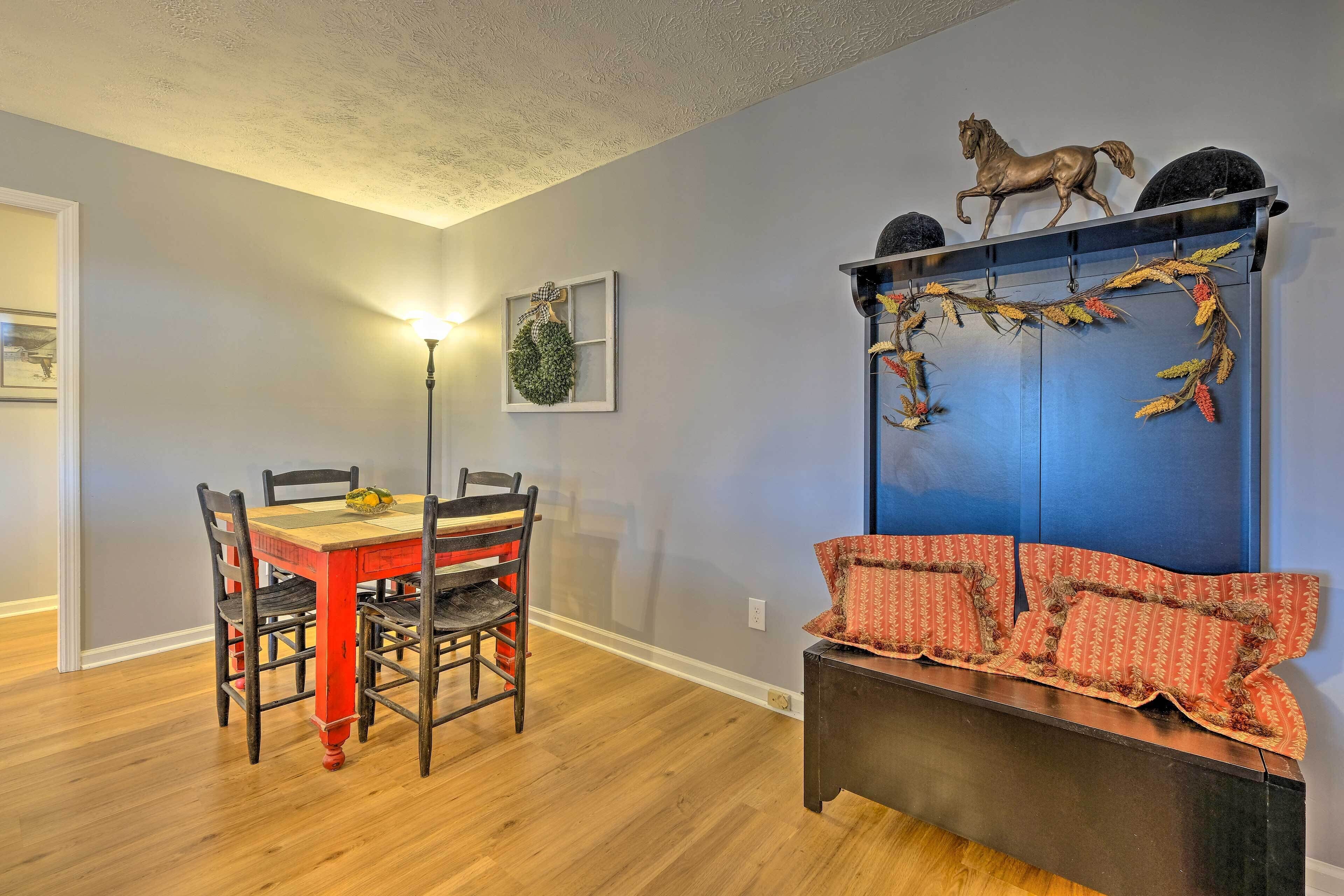 A dining area with a wooden table and chairs, a bench with patterned cushions, a wall-mounted horse sculpture, and a wreath on the wall.