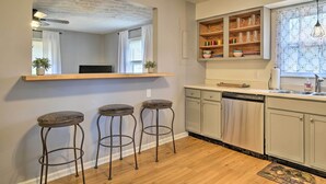 A kitchen with a wooden bar stool area, a dishwasher, and a window with patterned curtains. - Peaceful Bluegrass Getaway on 10-acre Farm! (Harrodsburg)