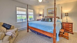 A bedroom with a four-poster bed, a nightstand with drawers, a lamp, a chair, and a window with blinds. - Peaceful Bluegrass Getaway on 10-acre Farm! (Harrodsburg)