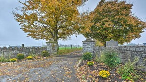 A stone gate with a plaque, surrounded by autumn foliage and a stone wall. - Peaceful Bluegrass Getaway on 10-acre Farm! (Harrodsburg)