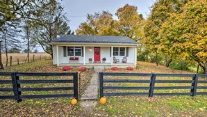 A white house with a red door, a porch with two chairs, and a fenced yard with pumpkins. - Peaceful Bluegrass Getaway on 10-acre Farm! (Harrodsburg)