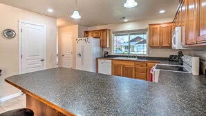 A kitchen with granite countertops, wooden cabinets, a refrigerator, a dishwasher, and pendant lighting.