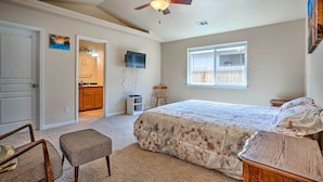 A bedroom with a bed, a ceiling fan, a window, and a door leading to a bathroom.