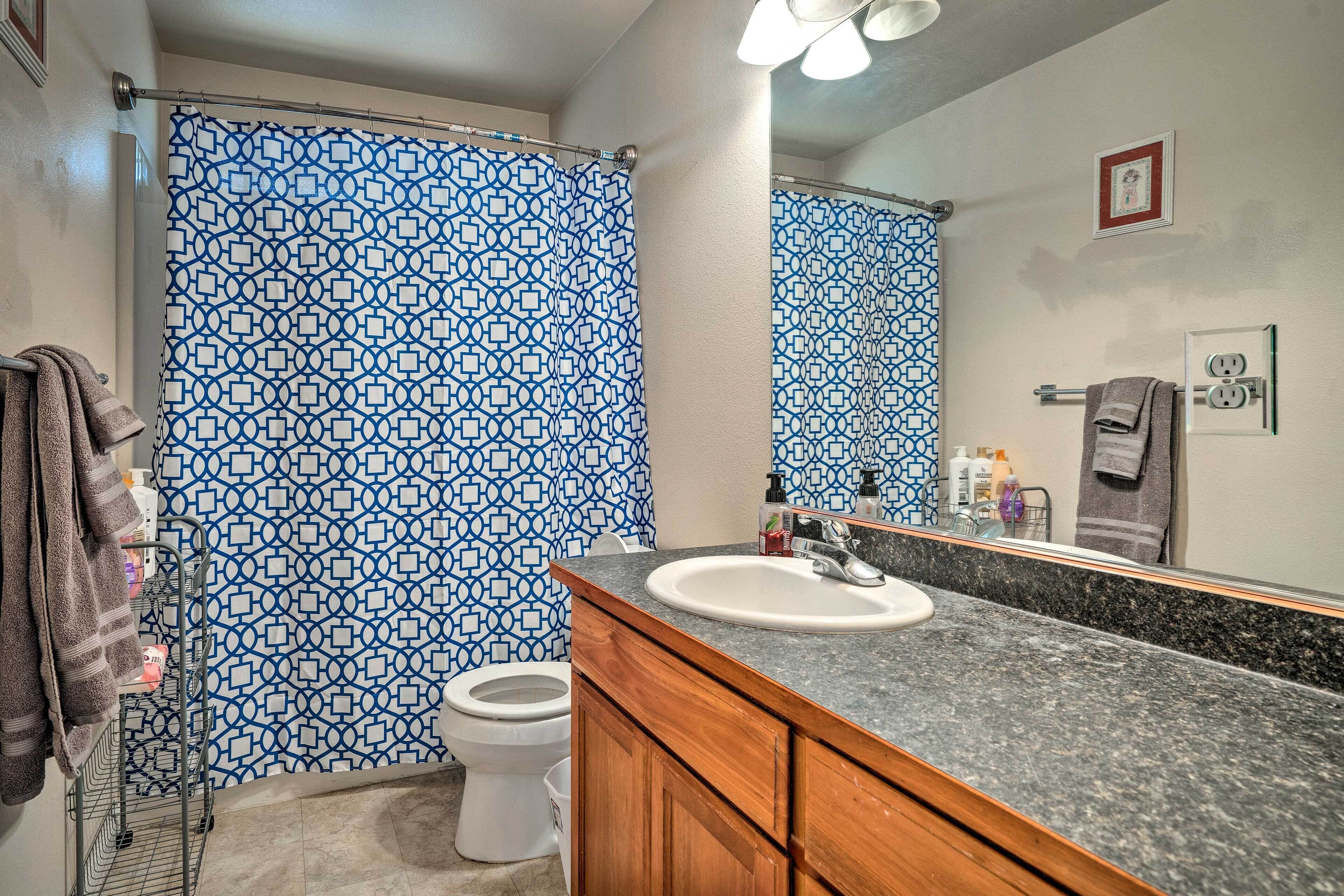 Un baño con cortina de ducha estampada, inodoro blanco, lavamanos con espejo y armarios de madera.