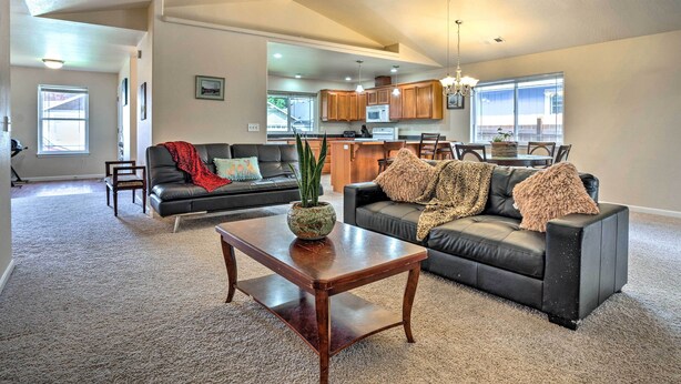 A spacious living room with a dark leather sofa, a wooden coffee table, and a view into the kitchen area.