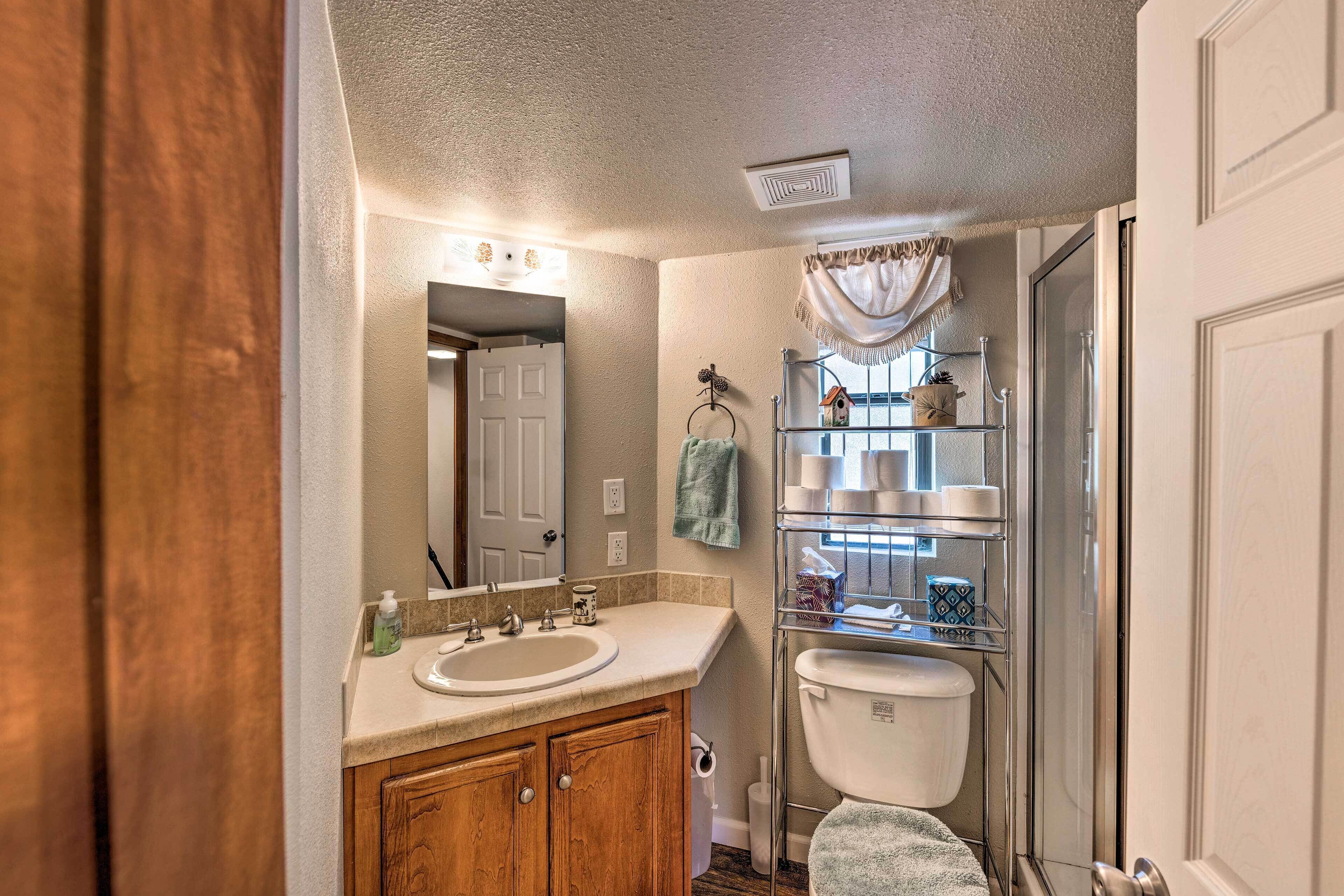 A bathroom with a wooden vanity, a white sink, a mirror, a towel rack, and a shower enclosure.