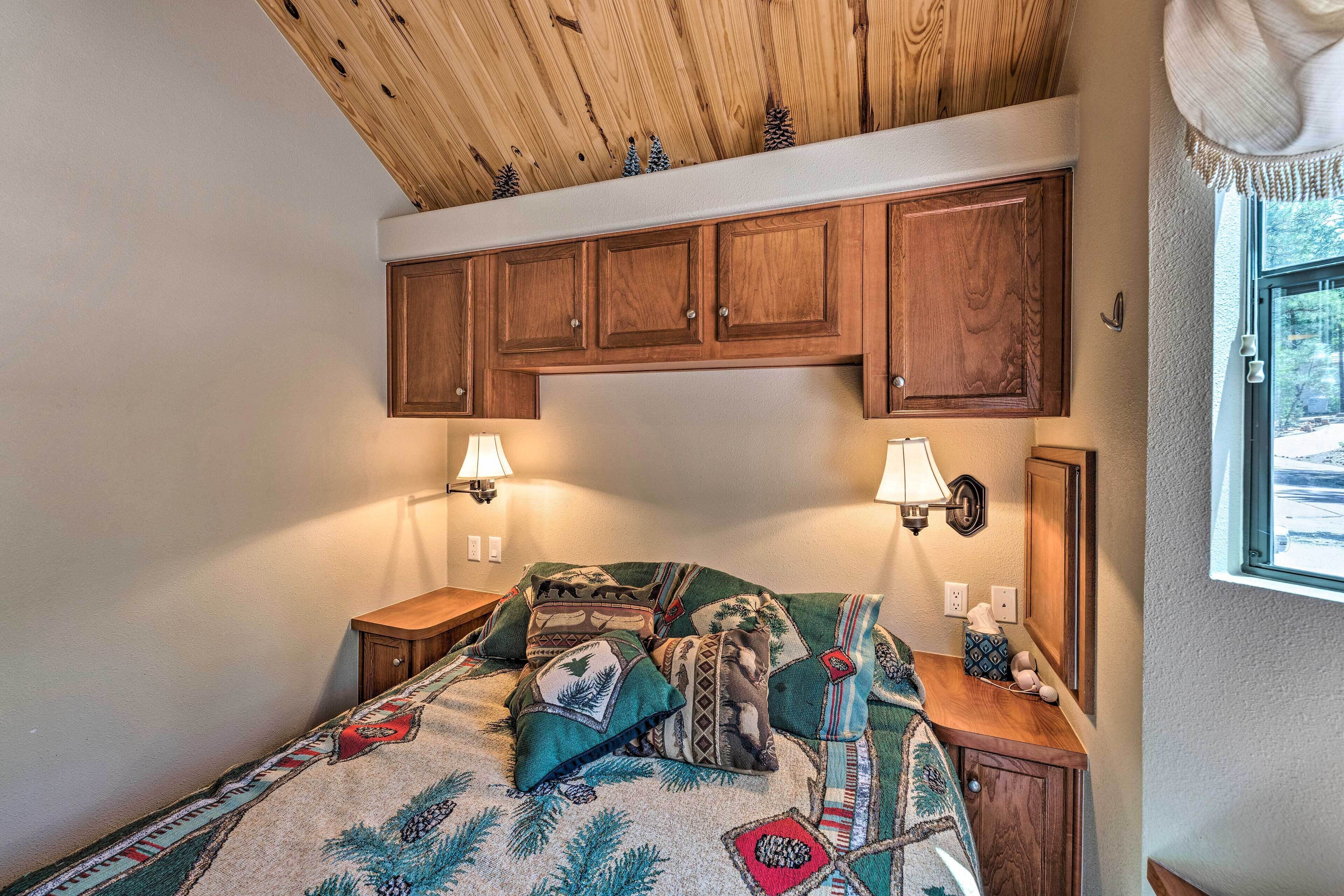 A bedroom with wooden cabinets above the bed, two bedside lamps, and a window with a view.