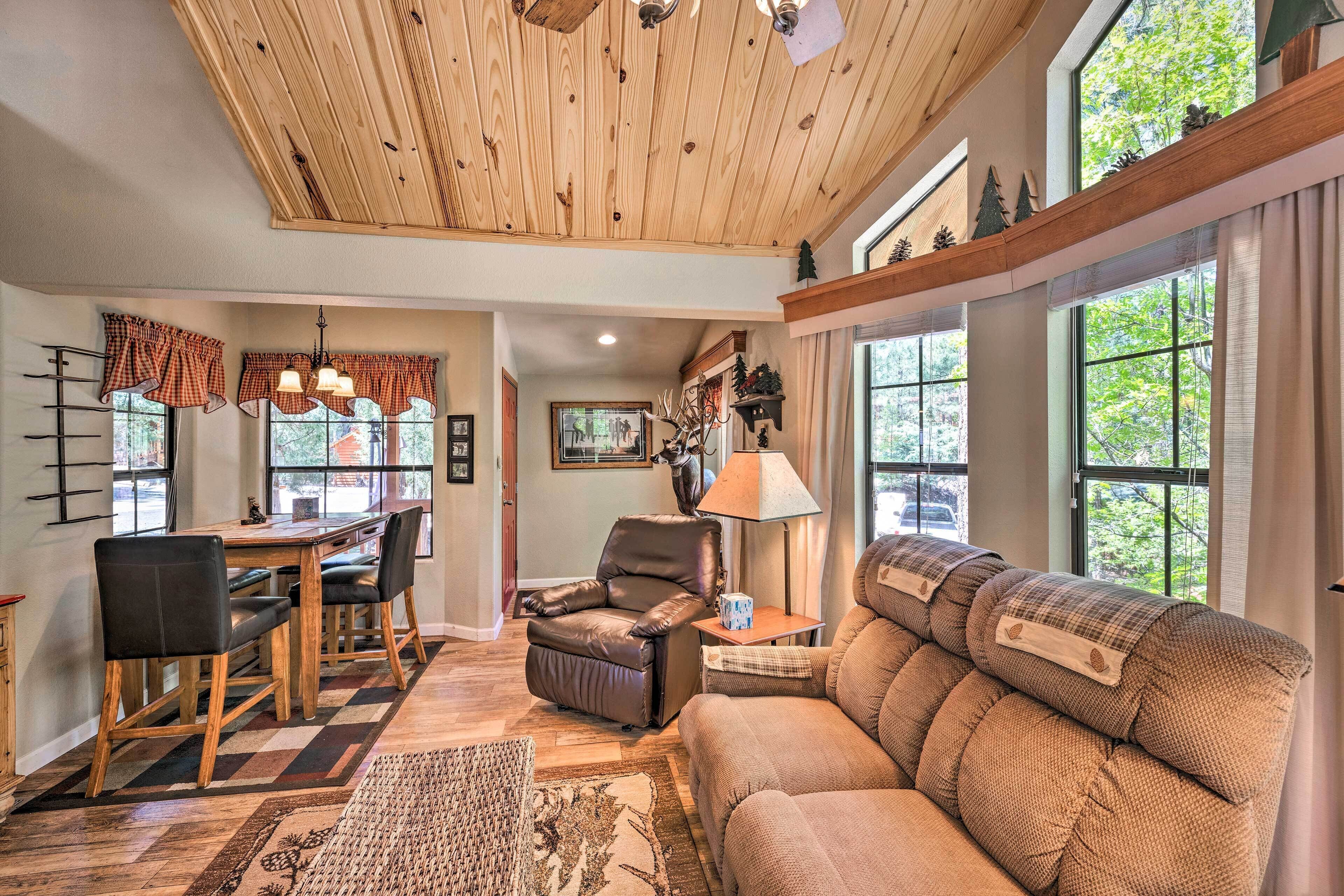 A cozy living room with a wooden ceiling, a fireplace, a sofa, and a dining area with a table and chairs.