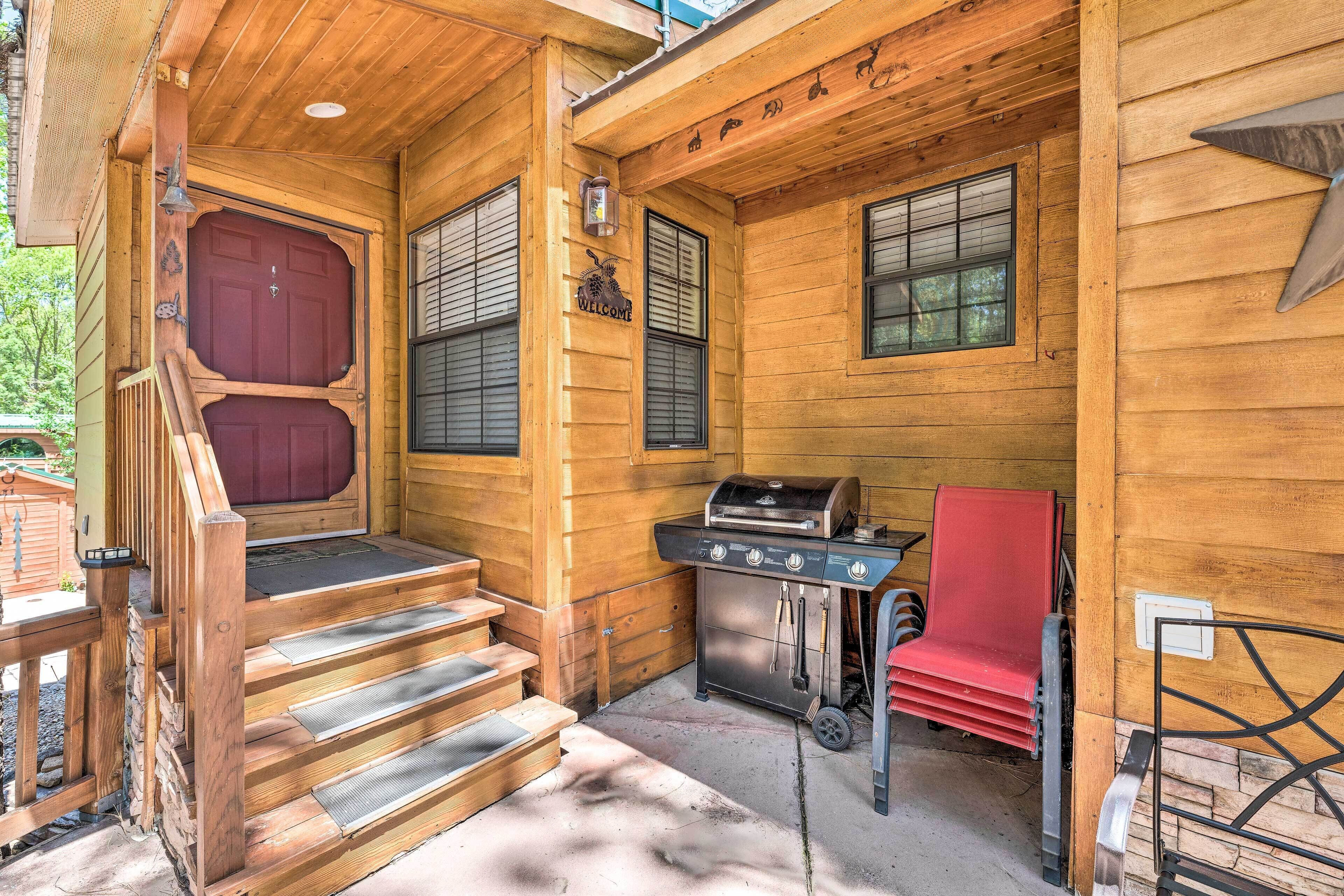 Una baita di legno con una porta rossa, un barbecue e una sedia rossa.