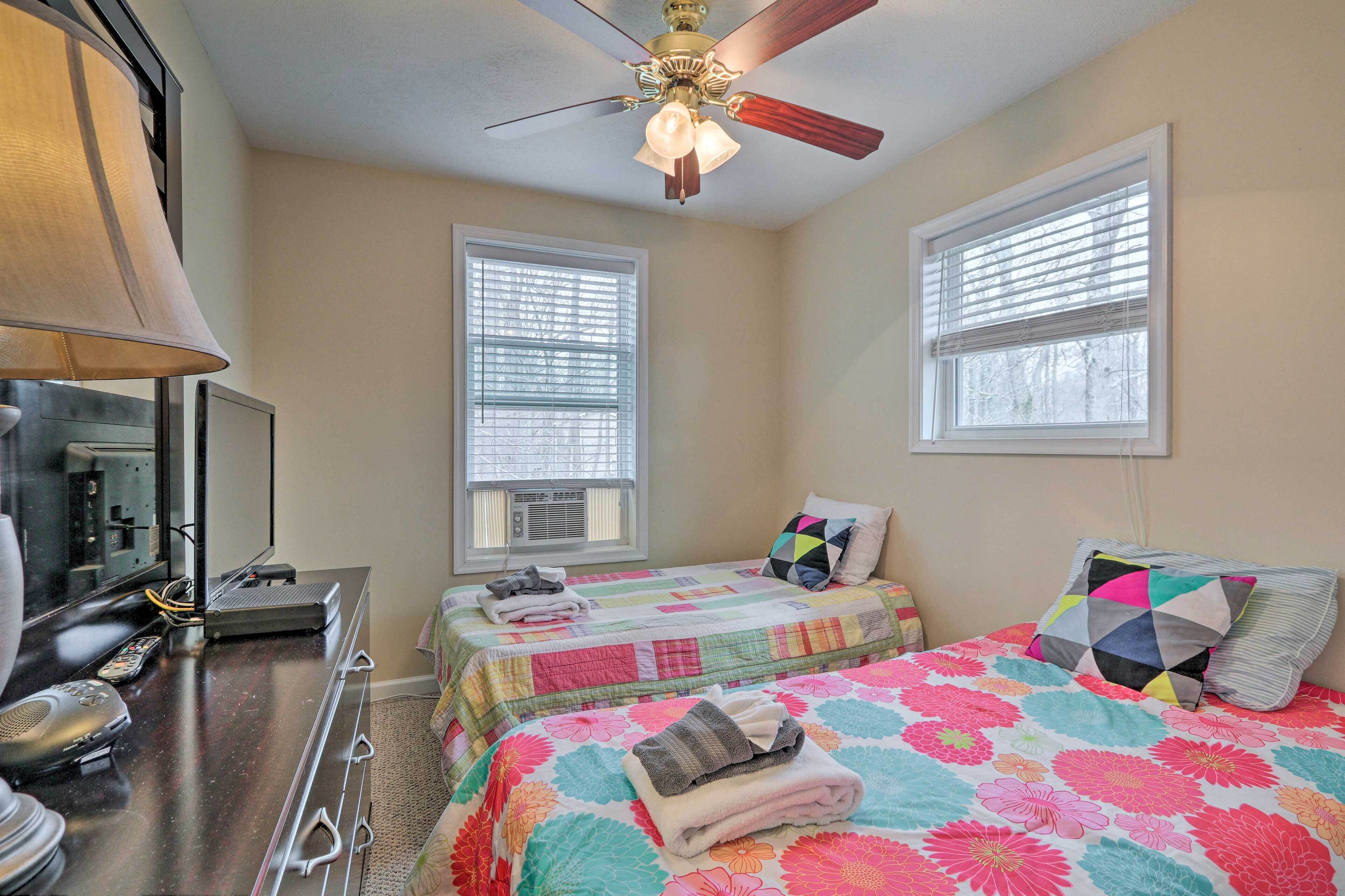 A bedroom with two beds, a ceiling fan, a dresser, and a TV.