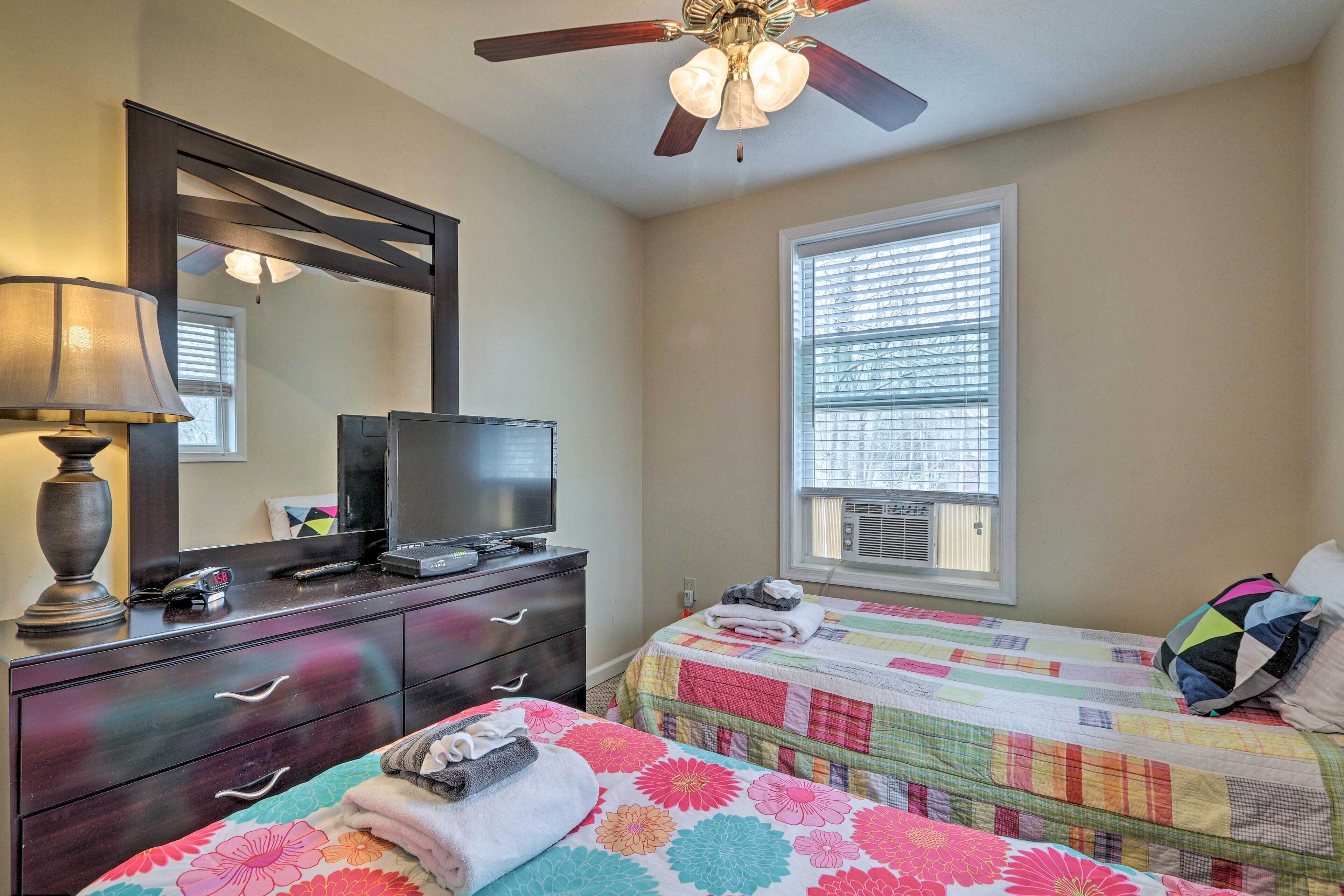 A bedroom with two beds, a dresser, a television, and a ceiling fan.