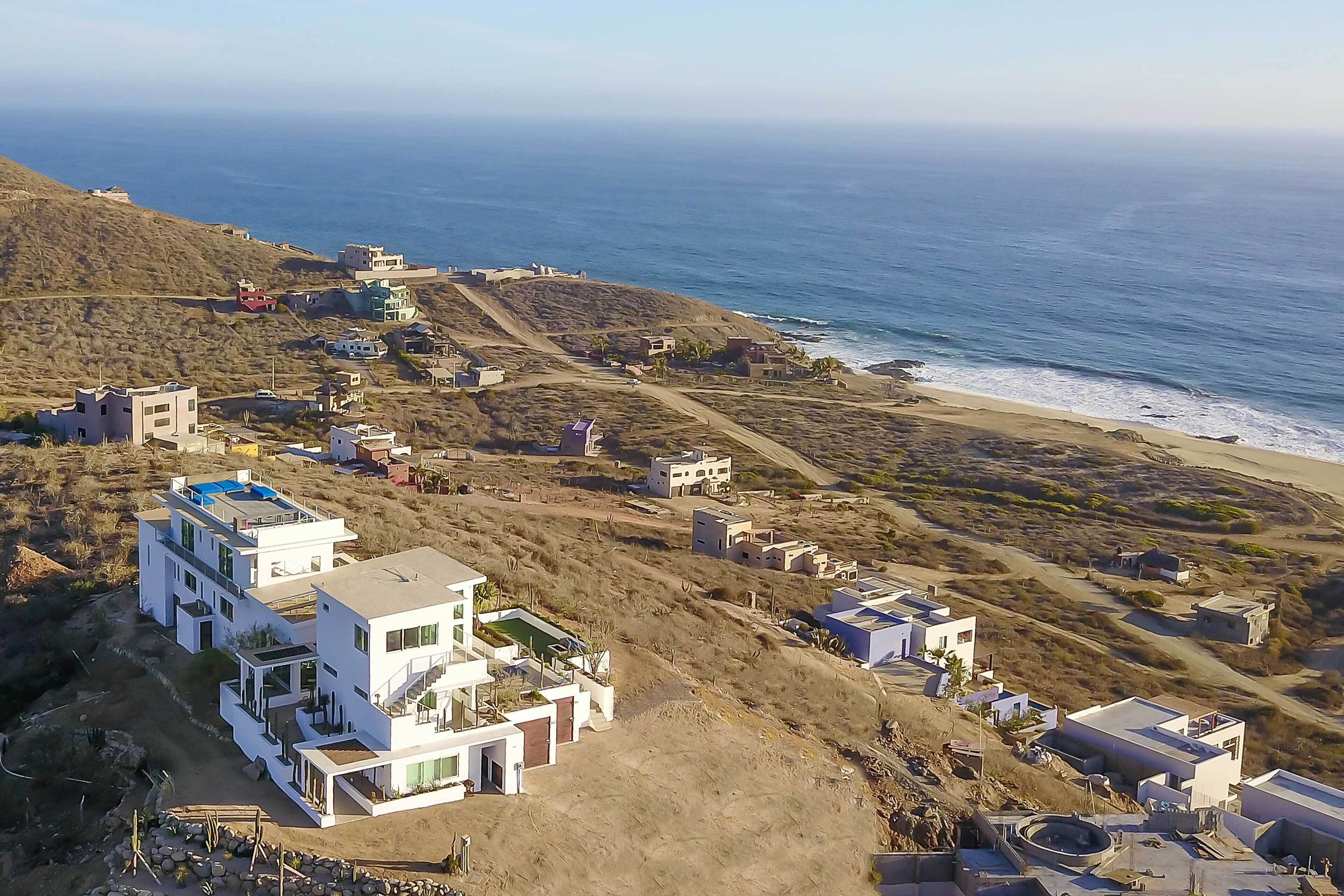 A coastal residential area with modern houses, a beach, and a hilly landscape.