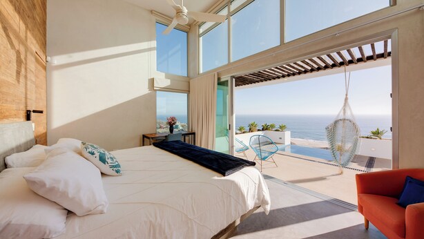A bedroom with a large bed, a ceiling fan, and a view of the ocean.