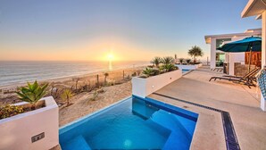 A pool area with a view of the beach and ocean at sunset.