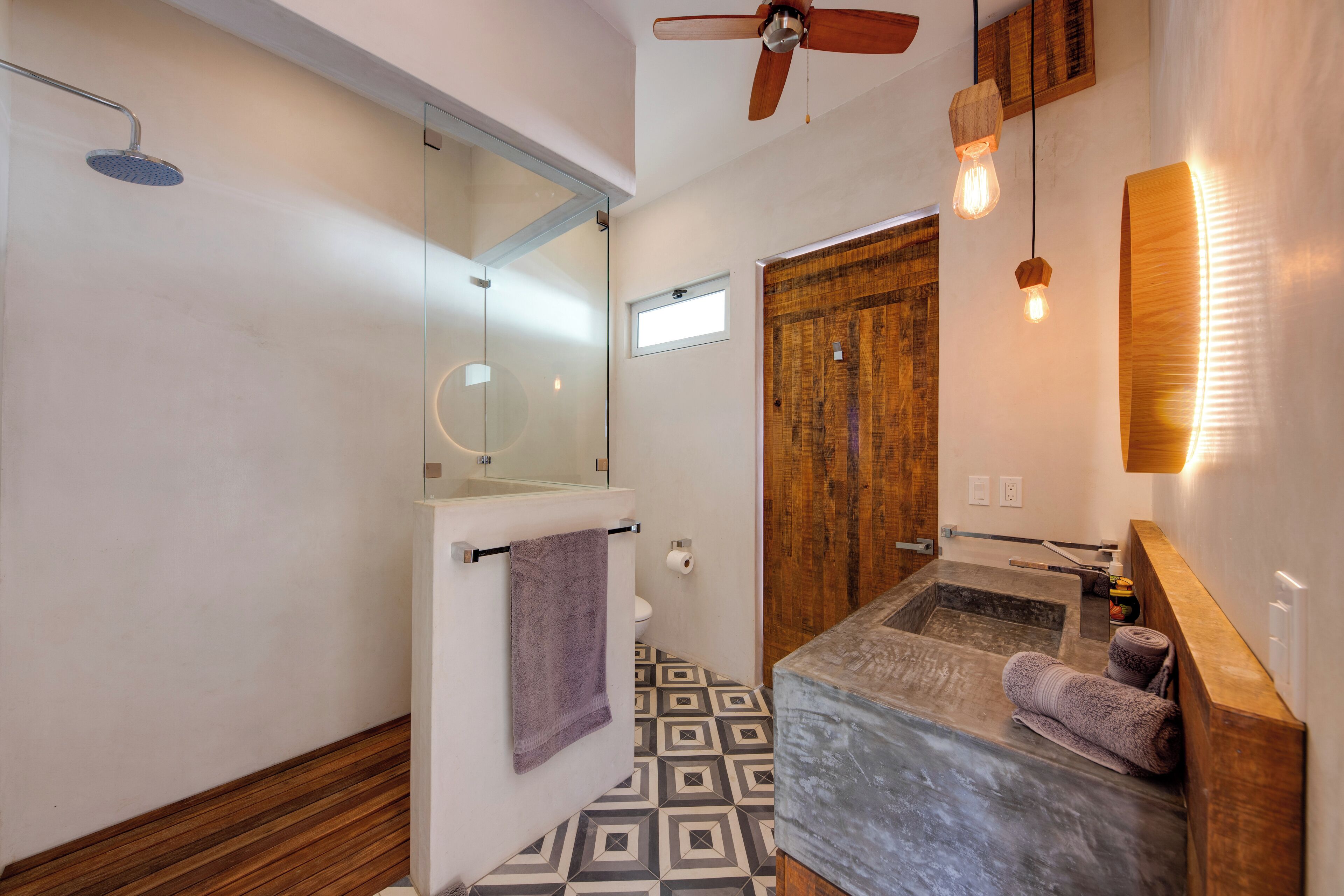 A modern bathroom with a shower, a toilet, a bidet, and a bathtub. There is a ceiling fan and pendant lights.