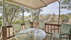 A covered outdoor seating area with a round table and striped chairs, overlooking a natural landscape with trees and a body of water. - Fishing Paradise w/ Deck On Suwannee River (Branford)