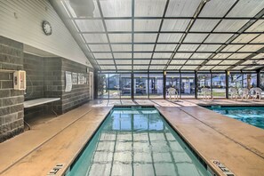 Une piscine intérieure avec un sol carrelé, une horloge au mur et un espace abrité avec des chaises.