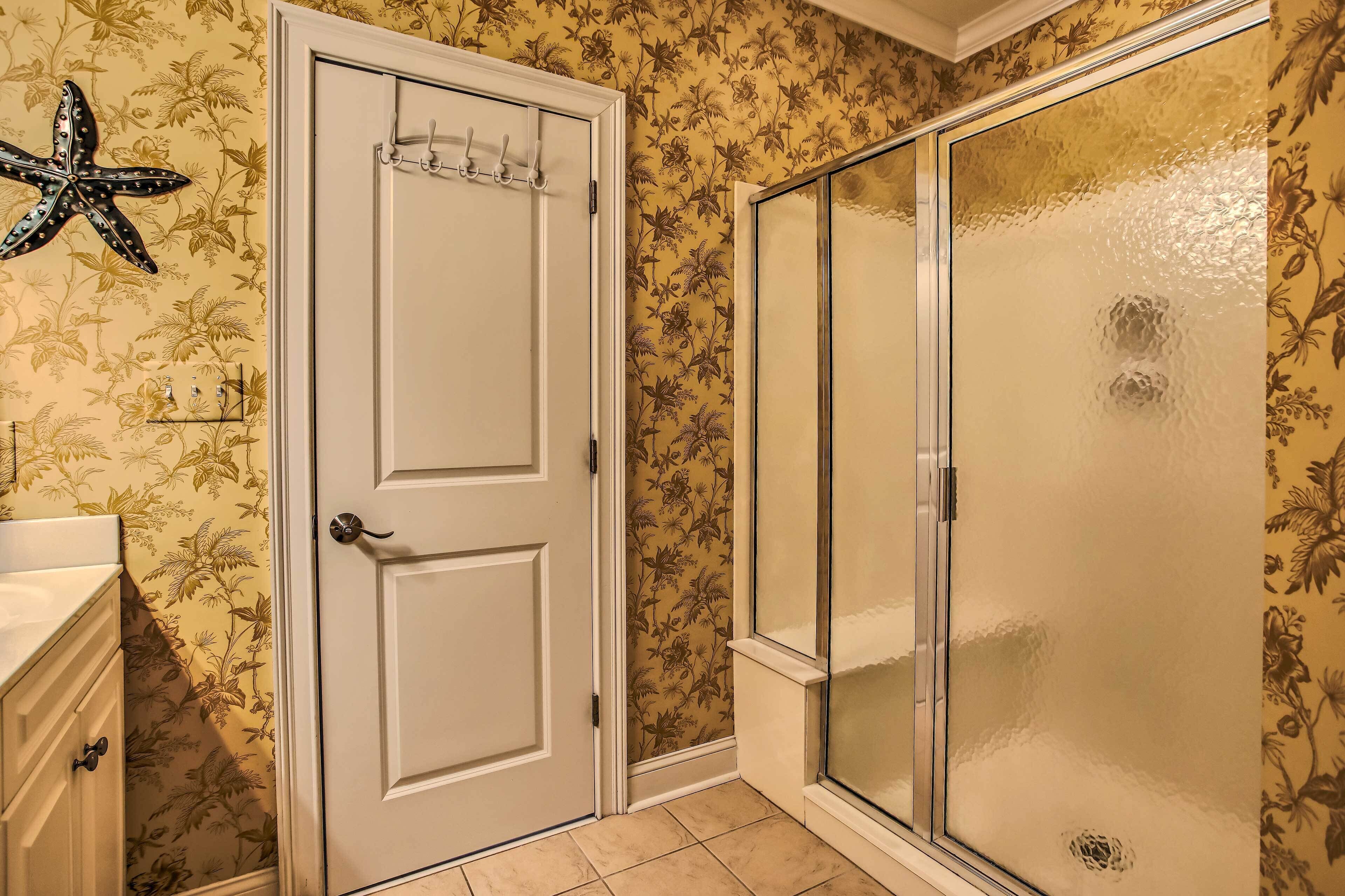 Une salle de bain avec une porte blanche, une douche avec une paroi en verre dépoli et un papier peint à motifs floraux.