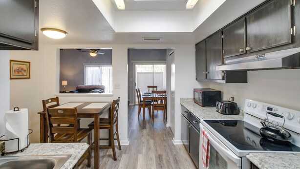 A modern kitchen with dark cabinets, a white countertop, and a dining area with wooden chairs and a table. - 4 Mi to Mill Ave: Family Retreat w/ Patio in Tempe (Tempe)