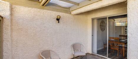 A covered patio with two wicker chairs, a ceiling fan, and a sliding glass door leading to an interior dining area.