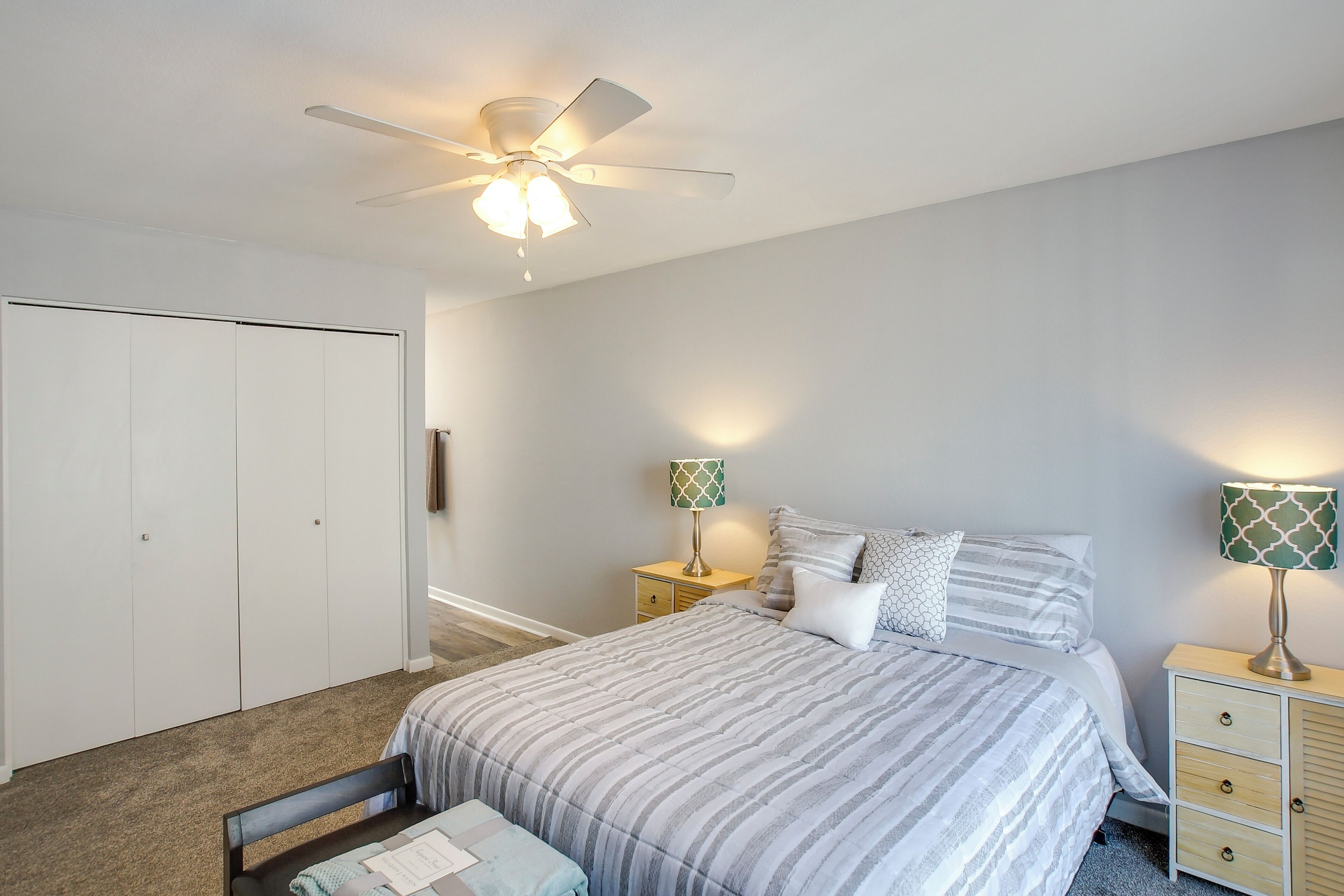 Une chambre à coucher comprenant un lit, une table de chevet, une lampe, un ventilateur de plafond et une armoire.