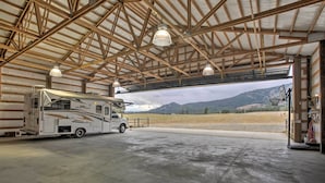 Ampio spazio per il ricovero di camper, con un camper di grandi dimensioni all'interno, pavimento in cemento e vista su un paesaggio montuoso attraverso un'apertura del garage.